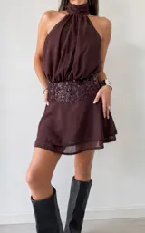 Vestido corto color bordó con cuello halter fruncido y falda con vuelo. Presenta una banda ancha en la cintura con textura plisada y detalles de lentejuelas brillantes en el mismo tono.