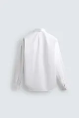 Camisa de manga larga, color blanco, con cuello italiano y corte slim fit. Presenta cierre frontal de botonadura y puños con botón.