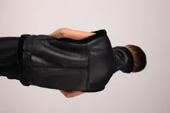 Chaleco negro de eco cuero con cuello y borde de gamulan. Tiene cierre cruzado con cremallera y cinturón con hebilla en la cintura.