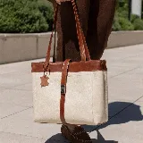 Bolso tipo tote de cuero color marrón con detalles en negro. Tiene doble asa de hombro y correa extraíble regulable. Incluye cierre principal y bolsillo interior.