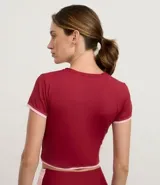 Remera deportiva cropped de manga corta, color rojo oscuro, con cuello redondo y ribetes contrastantes en blanco en el cuello y los puños. Presenta una pequeña inscripción en el pecho.