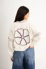 Campera oversize color crudo de algodón con spandex, corte de largo intermedio, mangas largas con detalles de costuras en zigzag bordadas y un gran diseño bordado a mano de una flor en la espalda.