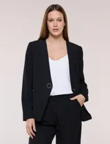 Blazer de sastrería color beige, sin solapas, con cuello en V profundo y cierre frontal de un único botón circular metálico en contraste.