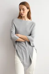 Capa tejida en hilo de lurex color beige, con cuello bote y diseño asimétrico de corte fluido.