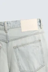 Jeans de mezclilla, tiro medio, color celeste claro lavado con efecto desgastado y roturas pronunciadas en ambas piernas. Corte ancho y relajado.
