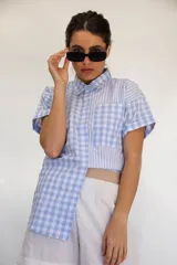 Camisa de manga corta con combinación de patrones a rayas y cuadros en tonos celeste y blanco, con bolsillo frontal aplicado y cierre de botones.