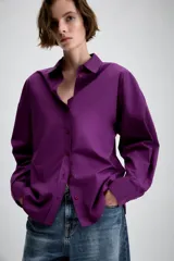 Camisa de manga larga en color violeta, con cuello solapa y cierre frontal de botones. Presenta un diseño de corte recto con detalle de pliegues en la espalda.