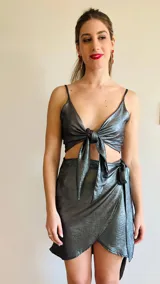 Conjunto de dos piezas color plateado brillante, compuesto por un top atado en el frente con escote en V y una minifalda cruzada con dobladillo asimétrico.