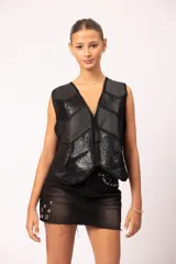 Pollera de jean negro con efecto de lavado localizado, terminación desflecada en el ruedo, tachas cuadradas en la cintura, apliques de alfileres de gancho en el bolsillo y ojalillos metálicos decorativos en la parte inferior.