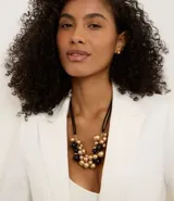 Conjunto de bijouterie compuesto por un collar con cordón negro ajustable y dije de esferas en tonos dorado y negro, acompañado por un par de aros tipo botón en tono dorado.