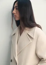 Abrigo corto de corte recto y diseño cruzado, confeccionado en tejido mezcla de lana. Presenta cuello con solapas de muesca, cierre frontal con botones oscuros y dos bolsillos laterales. Cuenta con forro interior y mangas largas.