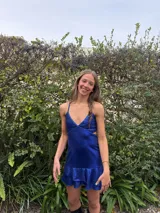 Vestido corto color bordó con escote en V, diseño de top triangular y aberturas laterales en la cintura. Presenta breteles finos cruzados en la espalda y falda con doble volado irregular en el ruedo.