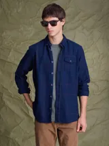 Camisa de manga larga en color azul noche con un patrón de cuadros finos en tonos rojos y verdes. Presenta cuello clásico, cierre frontal con botones y un bolsillo en el pecho con solapa.