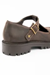 Zapato tipo guillermina de cuero lavado color marrón, con diseño de tira en T y cierre de hebilla metálica. Presenta costuras decorativas en contraste y suela de goma con plataforma dentada.