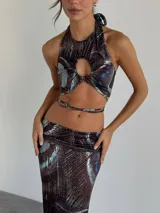 Top halter con estampado abstracto en tonos marrones y celestes, con abertura circular en el centro del pecho y lazos finos para atar en el cuello y la espalda.
