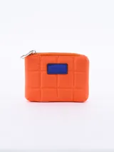 Monedero de diseño acolchado en color naranja, con cierre superior metálico y detalle de parche rectangular en color azul en el frente.