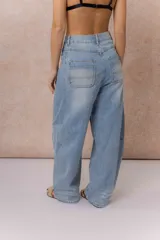 Jean de tiro alto con silueta balloon oversize, confeccionado en denim rígido de lavado celeste desgastado. Presenta costuras curvas que aportan volumen, cierre y botón frontal, y bolsillos funcionales.