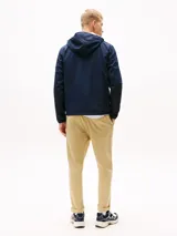 Campera cortavientos azul marino de corte amplio, con capucha fija, cuello alto, cierre de cremallera, dos bolsillos delanteros con cremallera y forro con diseño integral de la insignia de Tommy.