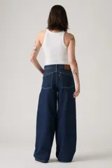 Jean de corte baggy y silueta barrel, confeccionado en denim rígido de color azul oscuro. Presenta costuras laterales curvadas que definen su forma característica, tiro alto y cierre frontal con botón y cremallera.