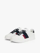 Zapatillas urbanas Tommy Hilfiger de corte bajo, confeccionadas en piel lisa color blanco. Presentan paneles laterales en azul marino y rojo, cordones oscuros y suela de goma gruesa con diseño dentado. Incluyen detalles de la marca en la lengüeta, lateral y talón.