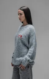 Sweater de punto texturizado color gris, con cuello redondo y diseño oversize. Presenta un bordado en relieve en la espalda con la frase 'art SUPPORT' en letras rojas y negras.