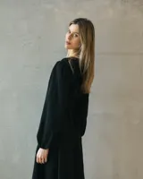 Vestido midi negro de silueta fluida, con mangas largas abullonadas y cintura marcada mediante un cinturón incorporado con hebilla metálica. Presenta un diseño de escote cerrado y caída liviana.