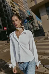 Camisa de cuello solapa y manga larga, con cierre frontal de botones y puños ajustables decorados con lazos del mismo tejido.