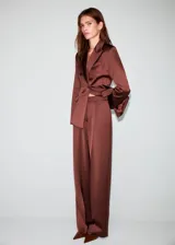 Pantalón largo de tiro medio en tejido satinado color marrón, con diseño de pernera recta, trabillas para cinturón, pinzas delanteras, bolsillos laterales y bolsillos de ribete en la parte posterior. Cierre frontal oculto con botón, gancho y cremallera.