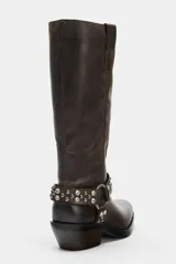 Bota de caña alta en piel color marrón oscuro, con detalle de tira con tachas y abalorios alrededor del tobillo, acabado en punta cuadrada y tacón plano.