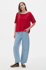 Remera oversized de manga corta en tejido rib blanco, con cuello redondo amplio ribeteado en negro. Presenta un pequeño parche rectangular con texto en la manga izquierda.