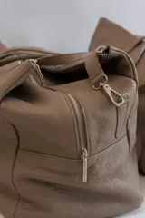 Bolso de viaje tipo weekender de cuero color marrón con doble asa de mano y correa bandolera ajustable y desmontable.