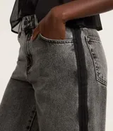 Pantalón de jean modelo wide leg, color gris lavado, con tiro alto, trabillas en la cintura y una banda lateral vertical en color negro que recorre toda la pierna. Cuenta con cierre tradicional y bolsillos.