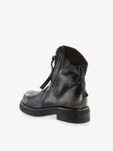 Bota corta de cuero bovino, color negro con efecto desgastado o metalizado grisáceo. Presenta cierre lateral con tirador y suela gruesa de goma con relieve.