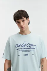 Remera celeste de manga corta con cuello redondo y estampado con la frase "Out of Office All Chasing Dream" en color negro.