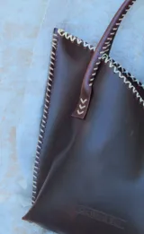 Cartera de cuero mediana con manijas largas, diseño con borde superior en corte en V y terminación artesanal con costuras contrastantes.