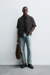 Camisa de manga corta con cuello bowling y calce relaxed fit, confeccionada en tejido seersucker elástico con textura. Presenta un diseño a rayas verticales en tonos oscuros y cierre frontal con botones.