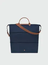 Bolso de viaje ampliable Longchamp modelo Le Pliage Original, color azul marino. Presenta diseño minimalista con asas cortas y correa larga ajustable en color marrón, cierre superior con solapa de cuero y botón a presión metálico.