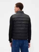 Chaleco puffer acolchado de color beige, con cierre frontal de cremallera, cuello alto y logo de la marca bordado en el pecho.