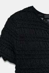 Top de punto negro con textura de nido de abeja, cuello redondo, mangas cortas y cierre frontal con botones.