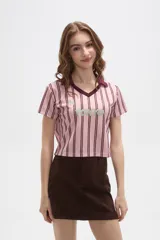 Remera estilo jersey de fútbol con corte cropped, cuello en V y mangas cortas. Presenta un diseño de rayas verticales en tonos rosados y bordó, con estampado frontal que incluye el texto 'TOKYO' y el número '24'.