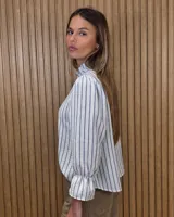 Blusa blanca de algodón con escote en V y cuello mao. Presenta mangas largas abullonadas con puños acampanados y fruncidos.