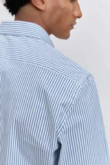 Camisa de corte regular, color celeste con rayas verticales blancas muy finas, cuello clásico y mangas largas con puños abotonados.