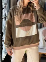 Buzo verde militar de calce relajado, confeccionado en friza de verano, con intervención artística artesanal en el frente mediante una composición abstracta de piezas textiles en tonos rosados, beige y marrón. Cuenta con cuello redondo, puños y dobladillo en rib elástico.