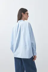 Camisa de manga larga en color celeste, con cuello mao y cierre frontal oculto. Presenta un diseño de silueta relajada con sisa caída y un bolsillo aplicado en el pecho.