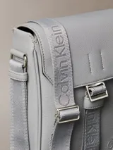 Cartera reporter Calvin Klein color gris, de diseño compacto con solapa frontal y correa ajustable para el hombro. Cuenta con detalles de marca grabados y correa central ajustable.
