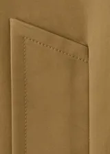 Chaqueta de corte amplio en tono tostado, con solapas y cuello de cuero sintético en color negro kontrastante. Posee cierre frontal de botones oscuros y bolsillos laterales discretos.