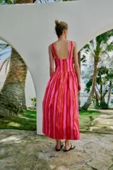 Vestido largo sin mangas con escote en pico y tirantes anchos. Presenta un diseño de rayas verticales en tonos fucsia y rojo, con detalle de falsos botones frontales y cierre de cremallera oculto en la espalda.
