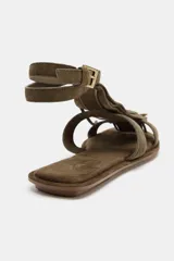 Sandalia plana color verde militar, con tiras de cuero y detalle de flecos en la parte delantera. Tiene pulsera al tobillo con cierre de hebilla metálica y punta redonda.