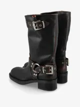Bota de caña media de cuero negro, estilo biker, con caña arrugada y detalles de correas con hebillas metálicas plateadas en la parte superior y alrededor del tobillo. Posee un taco bajo y grueso.