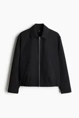 Campera negra de sarga con cuello camisero, cierre frontal y bolsillos insertados al bies. Presenta elástico revestido en puños y bajo, y un bolsillo interior.